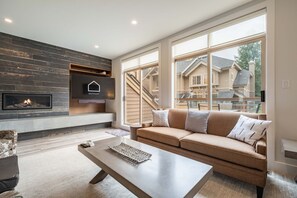 Una sala de estar moderna con chimenea, un sofá y ventanas amplias que dan a una casa.