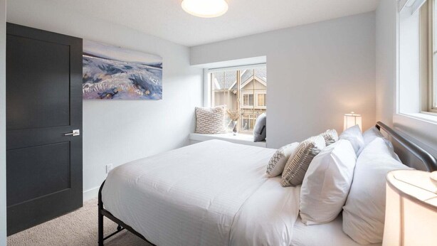 A bedroom with a bed, a window with a view, a door, and a ceiling light. - Luxury | Private garage | Private hot tub | BBQ (Whistler)