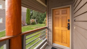 A wooden door with a keypad lock, a porch with a wooden railing, and a view of a well-maintained lawn and trees. - Luxury | Private garage | Private hot tub | BBQ (Whistler)