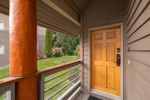 Eine Holztür mit Zahlenschloss, eine Veranda mit Holzgeländer und Blick auf einen gepflegten Rasen und Bäume.