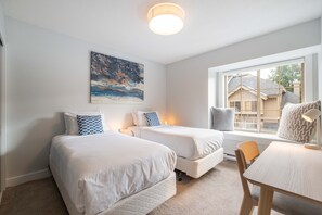 A bedroom with two beds, a desk, and a window with a view of houses. - Luxury | Private garage | Private hot tub | BBQ (Whistler)