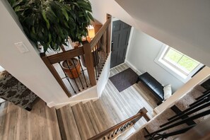 Una escalera de madera con una planta en el rellano, un banco y una puerta que da a otra habitación.