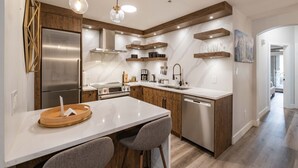 A modern kitchen with a stainless steel refrigerator, built-in oven, and dishwasher. There are wooden cabinets, a marble countertop, and pendant lighting. - Great location | Complex hot tub | BBQ | Pets (Whistler)