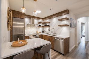 A modern kitchen with a stainless steel refrigerator, built-in oven, and dishwasher. There are wooden cabinets, a marble countertop, and pendant lighting. - Great location | Complex hot tub | BBQ | Pets (Whistler)