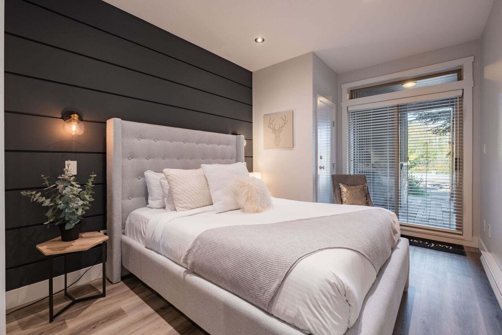 Um quarto moderno com uma cama grande, uma mesinha de cabeceira com uma planta e uma janela com persianas.