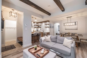A modern living room with a sectional sofa, a dining area with a wooden table, and a kitchen with pendant lighting. - Great location | Complex hot tub | BBQ | Pets (Whistler)