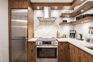 Une cuisine équipée d’un réfrigérateur en acier inoxydable, d’appareils électroménagers Bosch, de meubles en bois et d’un dosseret en marbre.