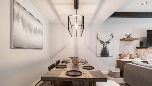 A modern dining area with a wooden table, black plates, and a pendant light. - Great location | Complex hot tub | BBQ | Pets (Whistler)