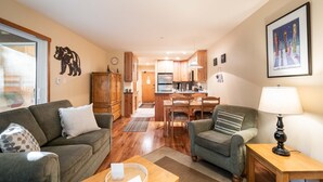 Un salón acogedor con sofá, sillón y mesa de centro, que conduce a una cocina y zona de comedor con armarios de madera y mesa.