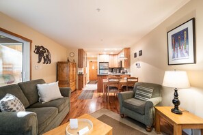 Ein gemütliches Wohnzimmer mit Sofa, Sessel und Couchtisch, angrenzend an eine Küche und einen Essbereich mit Holzausstattung und Esstisch.