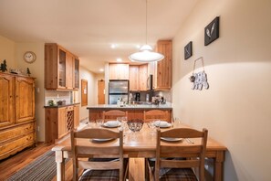 A compact kitchen with wooden cabinets, a stainless steel refrigerator, and a dining table set for four. - Close to Blackcomb | Shared hot tub | Free parking (Whistler)
