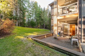 Ein modernes, zweistöckiges Gebäude mit Balkon, überdachter Außenbereich und Blick auf ein bewaldetes Gebiet.