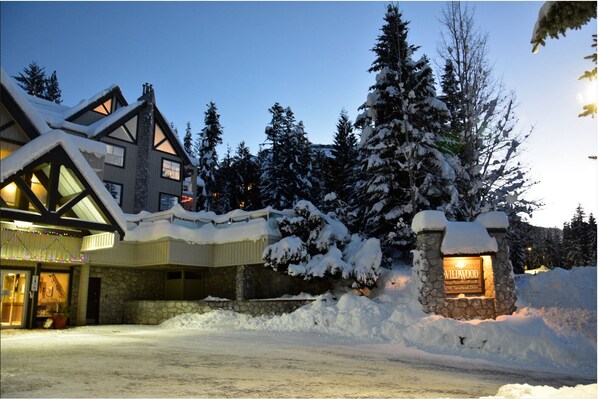 A snow-covered lodge with a stone entrance and a lit sign reading "Willamwood." - Close to Blackcomb | Shared hot tub | Free parking (Whistler)