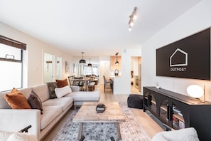 Ein modernes Wohnzimmer mit Sofa, Couchtisch und Kamin. Im Hintergrund ist ein Essbereich zu sehen, mit einer angrenzenden Küche.