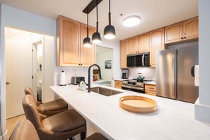 Une cuisine moderne avec des meubles en bois, des appareils en acier inoxydable, un plan de travail en marbre et des luminaires suspendus.