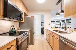 Eine moderne Küche mit Holzausstattung, einem Edelstahlkühlschrank, einem eingebauten Backofen und einer großen Kochinsel mit Spüle.