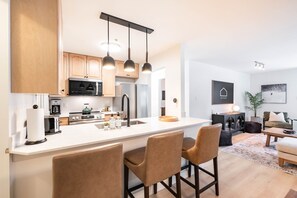 A modern kitchen with a central island, bar stools, and a dining area with a table and chairs. - Benchlands Townhome | Golf, Ski & Free Parking (Whistler)
