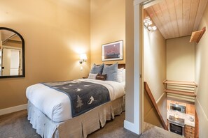 Ein Schlafzimmer mit einem Bett, einem Nachttisch, einer Wandleuchte, einem gerahmten Bild und einer Treppe, die in einen Küchenbereich führt.