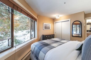 Ein Schlafzimmer mit großem Fenster, einem Bett, einem Schminktisch und einem Spiegel. Ein gerahmtes Bild ist ebenfalls zu sehen.