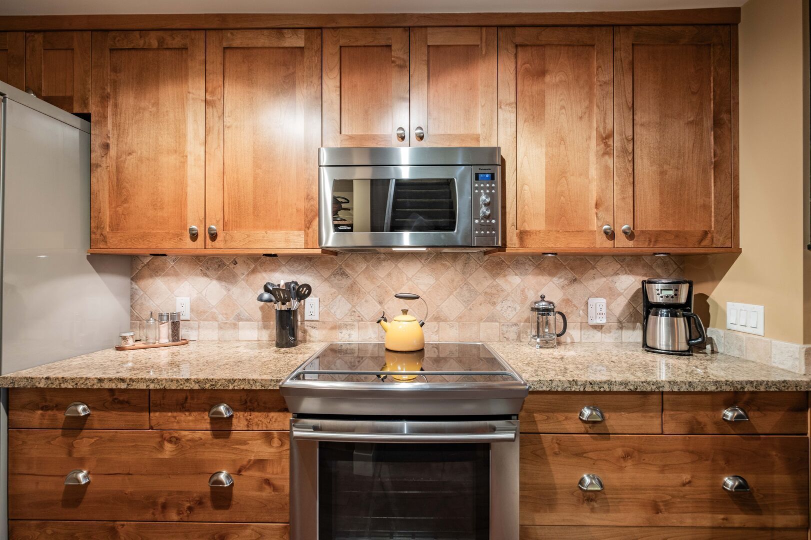 A kitchen with wooden cabinets, a stainless steel microwave, a coffee maker, and a kettle on the countertop.