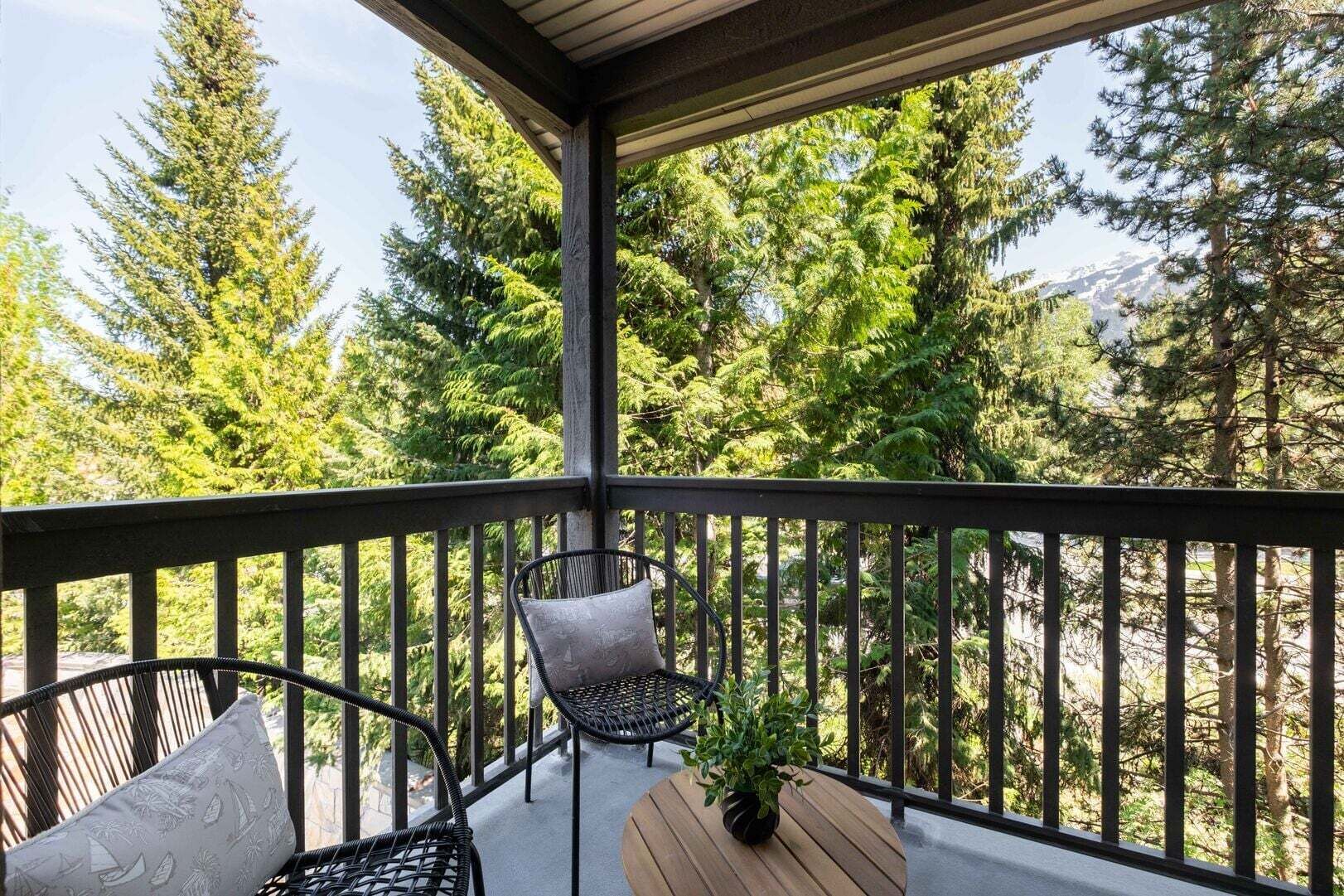 A balcony with a wooden table, two chairs, and a potted plant.