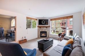 Ein Wohnzimmer mit Kamin aus Stein, einer Couch, einem blauen Sessel und einem Essbereich mit Tisch und Stühlen.