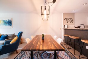 Ein moderner Essbereich mit Holztisch, weißen Stühlen, einer blauen Couch und einer Küchenzeile mit Barhocker.