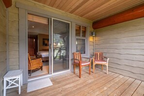 Een houten terras met een schuifdeur die leidt naar een slaapkamer met een bed en een rieten stoel.