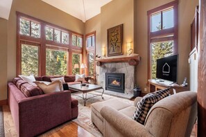 A cozy living room with a fireplace, comfortable seating, and large windows. - NEW Townhome | Private hot tub | Smart TV (Whistler)