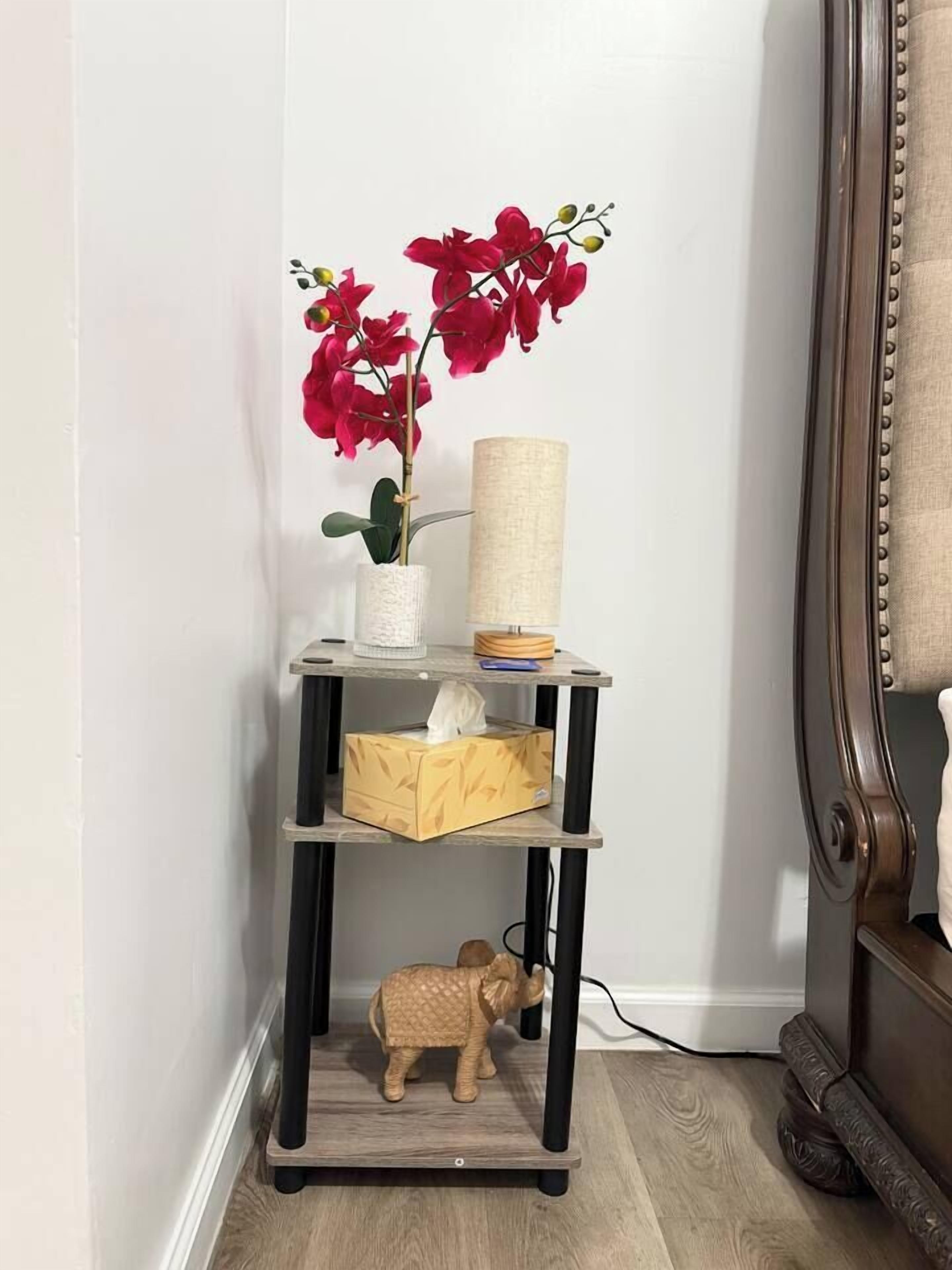 A corner with a wooden floor, a small wooden shelf with a plant, a lamp, and a tissue box.