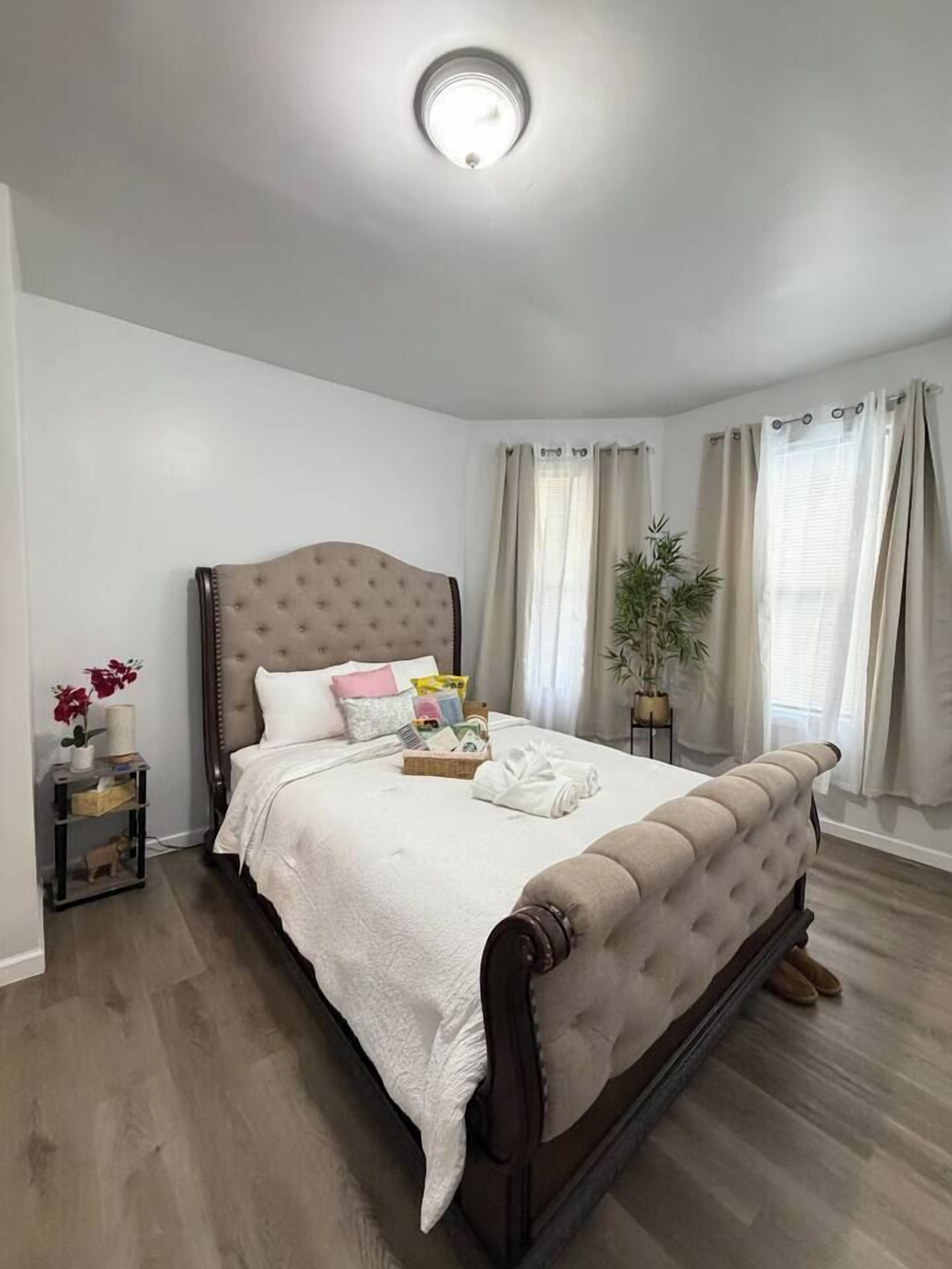 Un dormitorio con una cama grande, una mesita de noche, una planta en maceta y una ventana con cortinas.