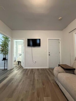 A living room with a flat-screen TV mounted on the wall, a sofa, and a wooden floor. - Renovated 3BR | Bay Windows | EWR 15 Min (East Orange)