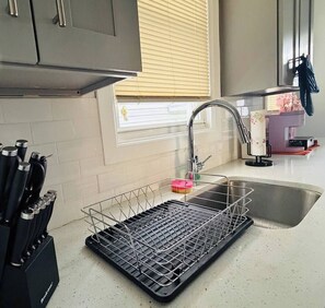 A kitchen with a sink, a dish rack, and a knife block. - Renovated 3BR | Bay Windows | EWR 15 Min (East Orange)