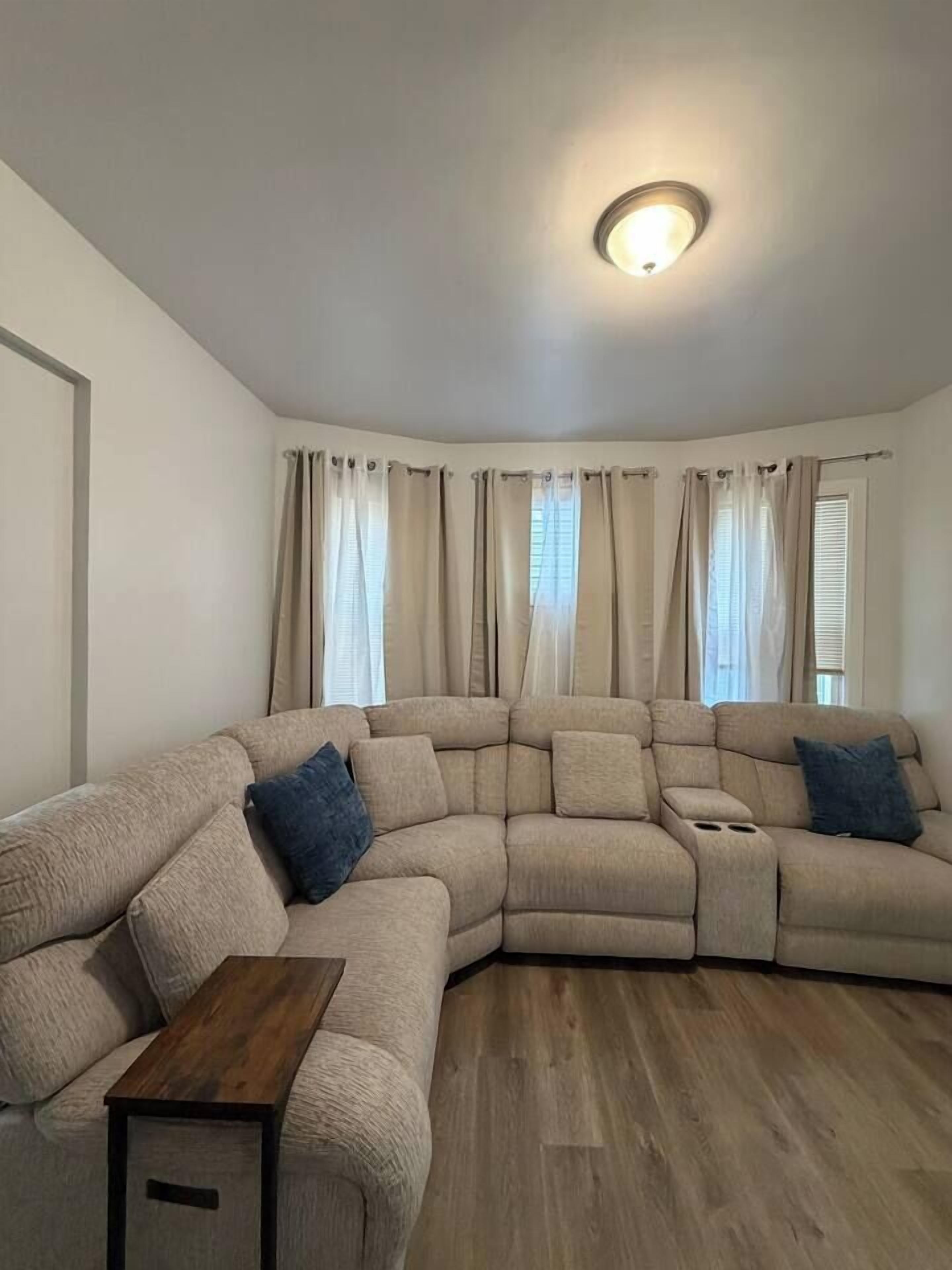Ein Wohnzimmer mit einem Ecksofa, einem Holztisch und einer Deckenleuchte.
