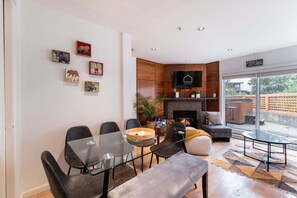 A modern living room with a glass dining table, comfortable seating, a fireplace, and a large window offering a view of the outdoors. - Townhome with Private Hot Tub & Pool (Whistler)