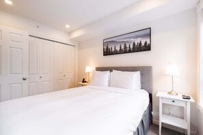 A neatly made bed with white linens, a grey headboard, and two bedside lamps. - Townhome with Private Hot Tub & Pool (Whistler)