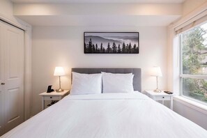 Une chambre à coucher avec un lit, deux tables de chevet, une commode, une fenêtre et un tableau au mur.
