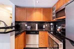A modern kitchen with wooden cabinets, a dishwasher, a stove, and a microwave. - NEW Townhome | Private hot tub | Complex pool (Whistler)
