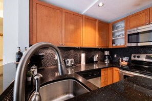 A modern kitchen with wooden cabinets, a stainless steel sink, a microwave, and a dishwasher. - Townhome with Private Hot Tub & Pool (Whistler)