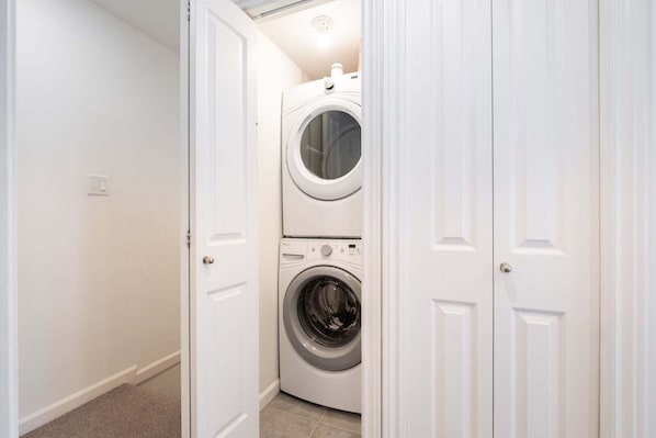 A laundry room with a front-loading washer and dryer, white walls, and a door leading to another room. - Townhome with Private Hot Tub & Pool (Whistler)