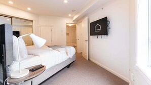 A hotel room with a bed, bedside table, lamp, remote control, and a mounted television. - NEW Townhome | Private hot tub | Complex pool (Whistler)