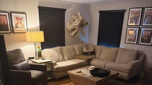 A living room with a sectional sofa, a coffee table, a side table with a lamp, and a wall-mounted sculpture. - Central R&R Cape Cod (Casper)