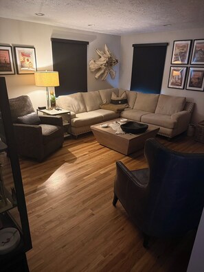Ein Wohnzimmer mit einem Ecksofa, einem Couchtisch, einem Beistelltisch mit Lampe und einer Wandskulptur.