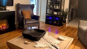 A living room with a fireplace, a leather armchair, a coffee table with decorative items, a television, and a bookshelf. - Central R&R Cape Cod (Casper)