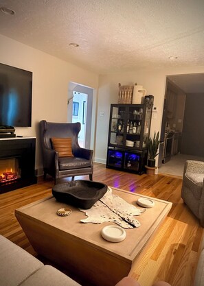 Ein Wohnzimmer mit Kamin, Ledersessel, Couchtisch mit Dekoration, Fernseher und Bücherregal.