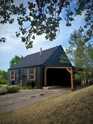 A single-story house with a dark green exterior, a sloped roof, and a garage. - Central R&R Cape Cod (Casper)