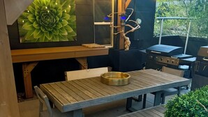 An outdoor dining area with a wooden table and benches, surrounded by greenery and a large flower mural. - Central R&R Cape Cod (Casper)