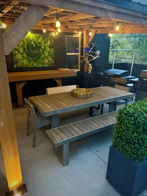 Ein Essbereich im Freien mit einem Holztisch und Bänken, umgeben von viel Grün und einer großen Blumenmalerei.