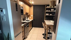 A modern kitchen with wooden cabinets, a built-in oven, and a dining area with a table and chairs. - Central R&R Cape Cod (Casper)