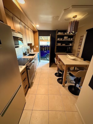 A compact kitchen with modern appliances, a dining area with a table and chairs, and a view into the living space. - Central R&R Cape Cod (Casper)